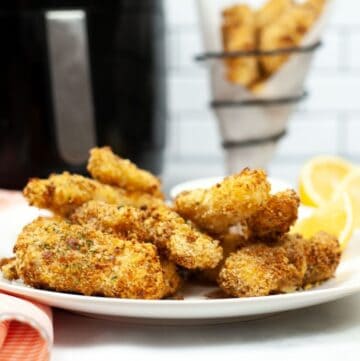 Panko Crusted fish sticks on a white plate with an air fryer in the background.