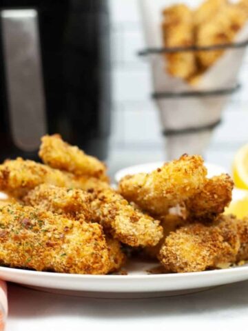 Panko Crusted fish sticks on a white plate with an air fryer in the background.