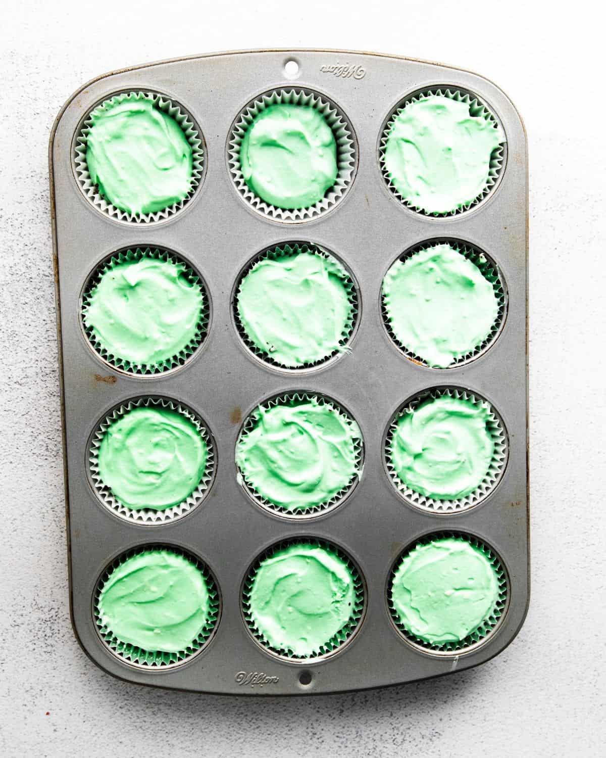 A 12 count muffin tin with green cream cheese in each tmold.