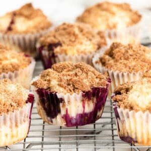 Streusel topped blueberry muffin sin a cupcake liners on a silver wire wrack.