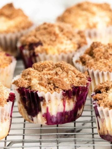 Streusel topped blueberry muffin sin a cupcake liners on a silver wire wrack.