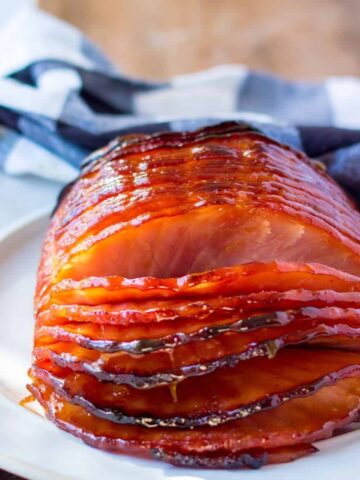 A sliced glazed ham on a plate with a blue and white checkered napkin behind it.