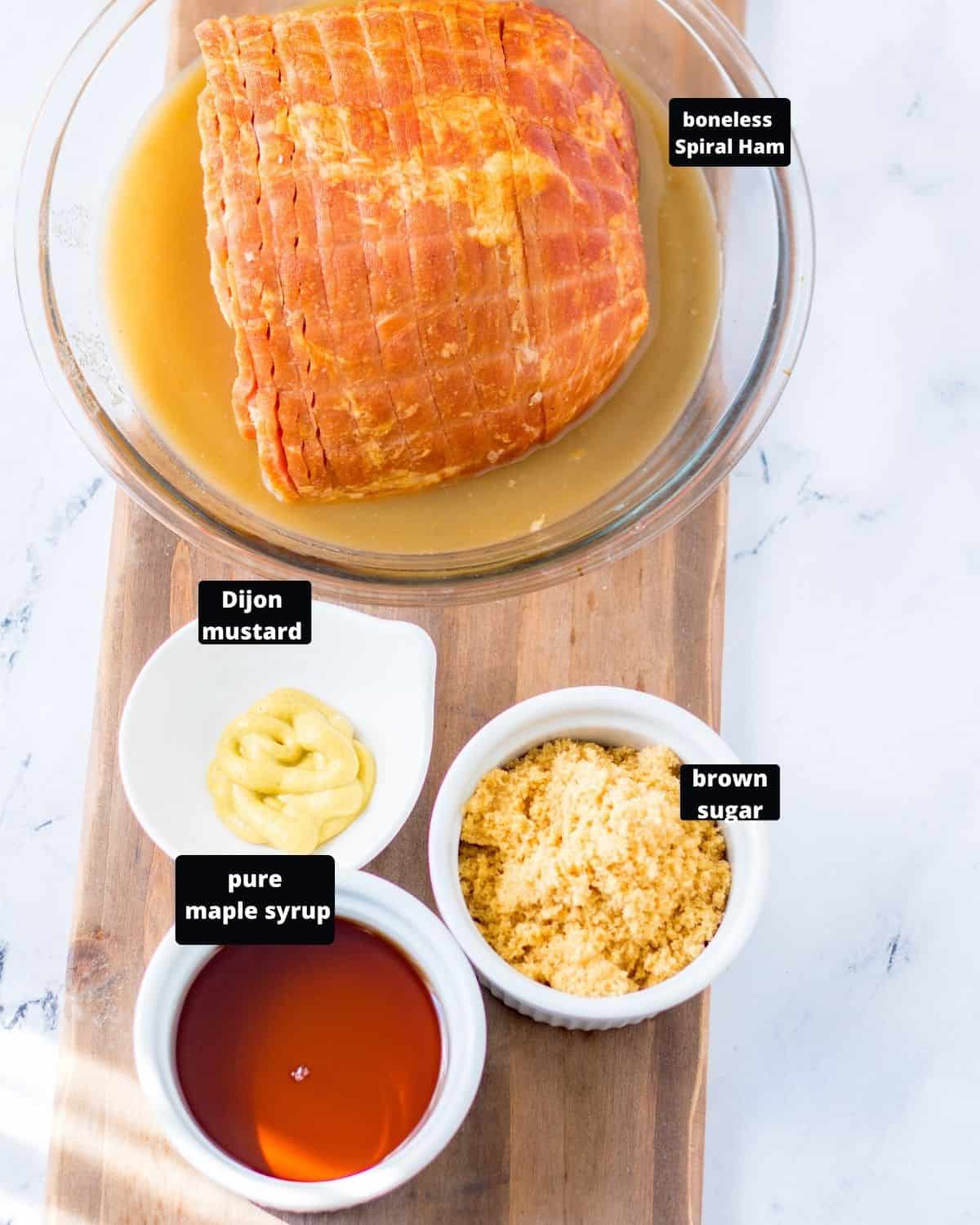 The ingredients to make a maple glazed ham, the boneless ham, maple syrup, brown sugar, and Dijon mustard on a board