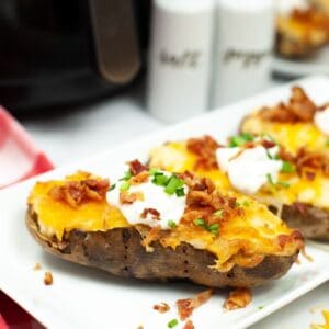 A side view of a potatoes on a white plate topped with cheese, bacon, sour cream, and chopped scallions.