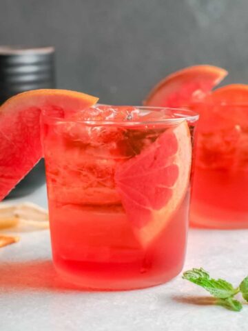 2 clear glasses filled with ice, aperol liquor and a wedge of fruit in the glass.