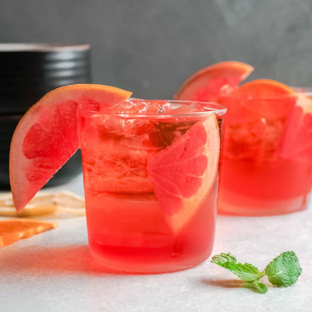 2 clear glasses filled with ice, aperol liquor and a wedge of fruit in the glass.