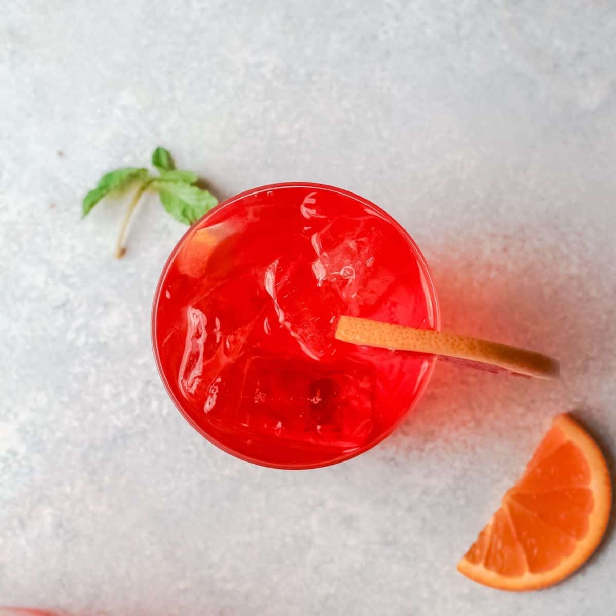 An overhead view of a bright orange cocktail with a wedge of orange on the rim.