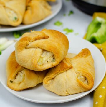 A trio of chicken stuffed crescent rolls on a plate with another plate behind it filled with chicken sandwiches.