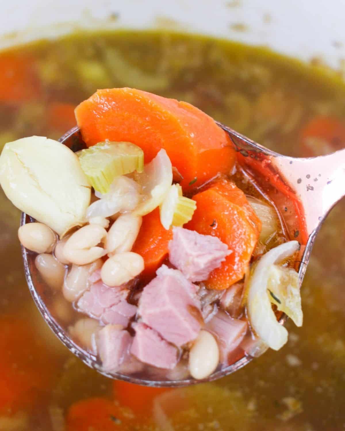 A ladle filled with diced ham, carrots, celery, and onions.