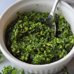 A white bowl with green basil kale pesto in it with a silver spoon in the bowl.