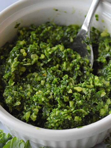 A white bowl with green basil kale pesto in it with a silver spoon in the bowl.