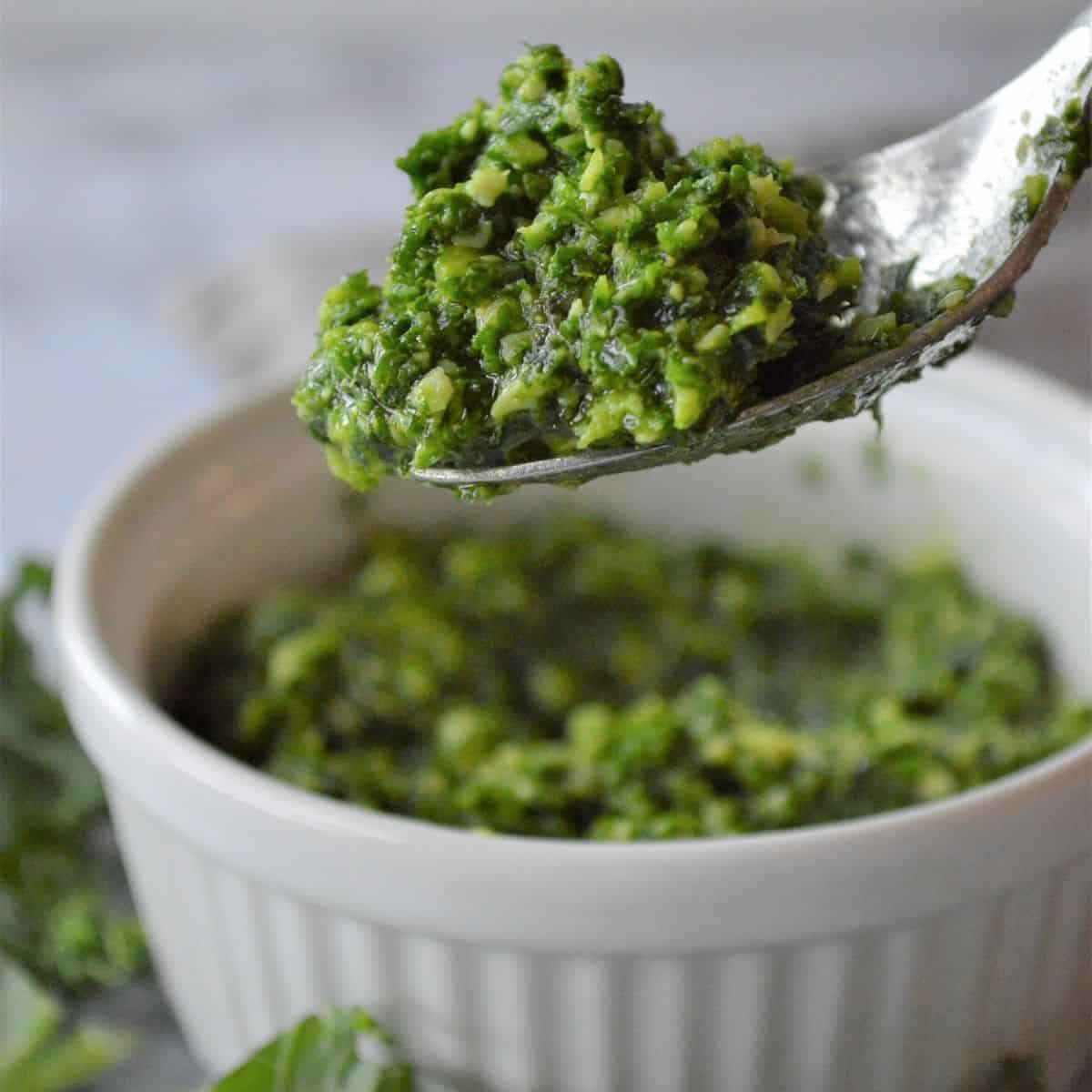 Homemade Kale pesto without nuts on a spoon being picked up out of a bowl.