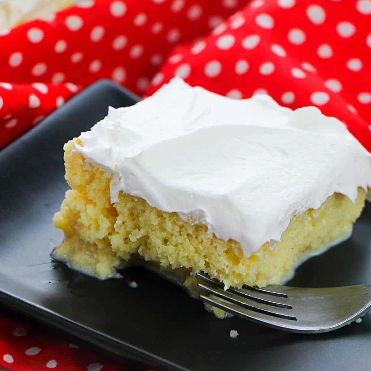 A slice of tres leche cake topped with whipped cream on a black plate.