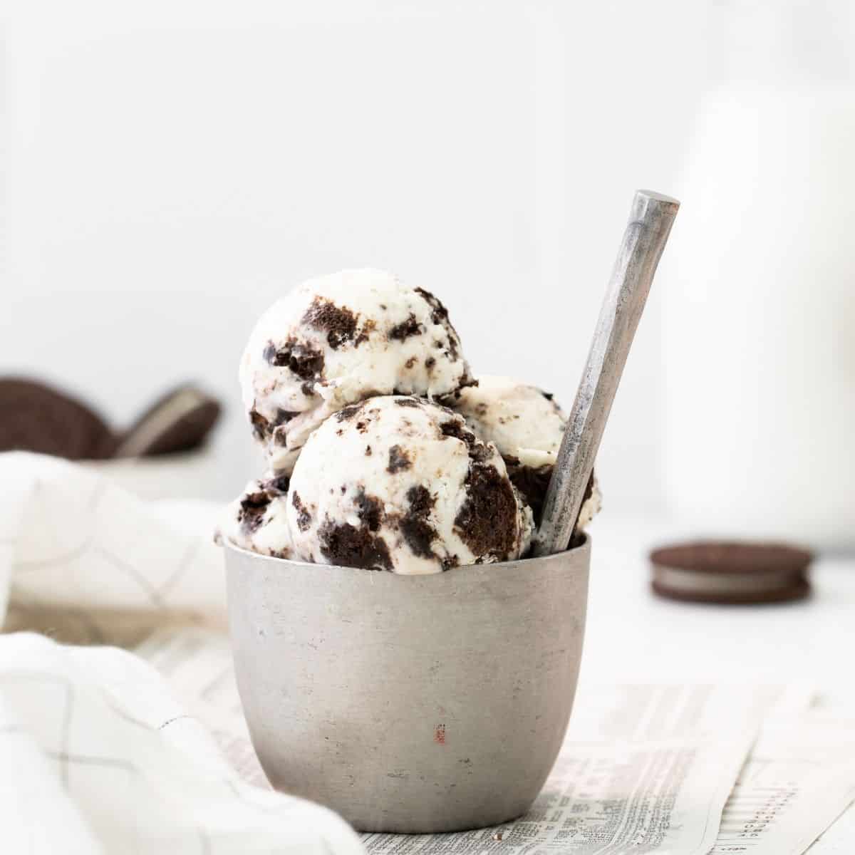 A silver bowl with scoops of cookies and cream ice cream on it.