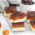 Layered homemade Caramel candy bars stacked on a wire rack.