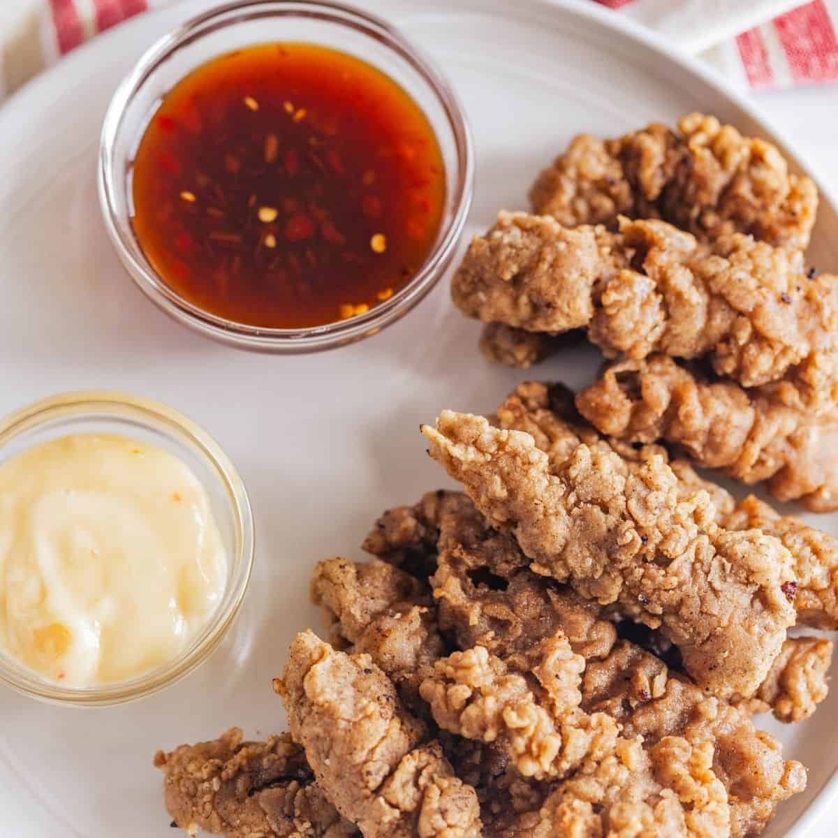 An overhead view of fingers steaks on a plate with Asian dipping sauces