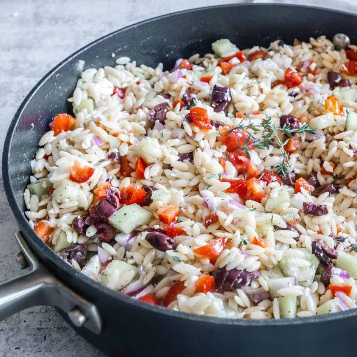 Greek Orzo Pasta Salad in a large pan with Kalamata olives, tomatoes, peppers. 