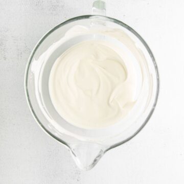 A white glass mixing bowl filled with whipping cream.