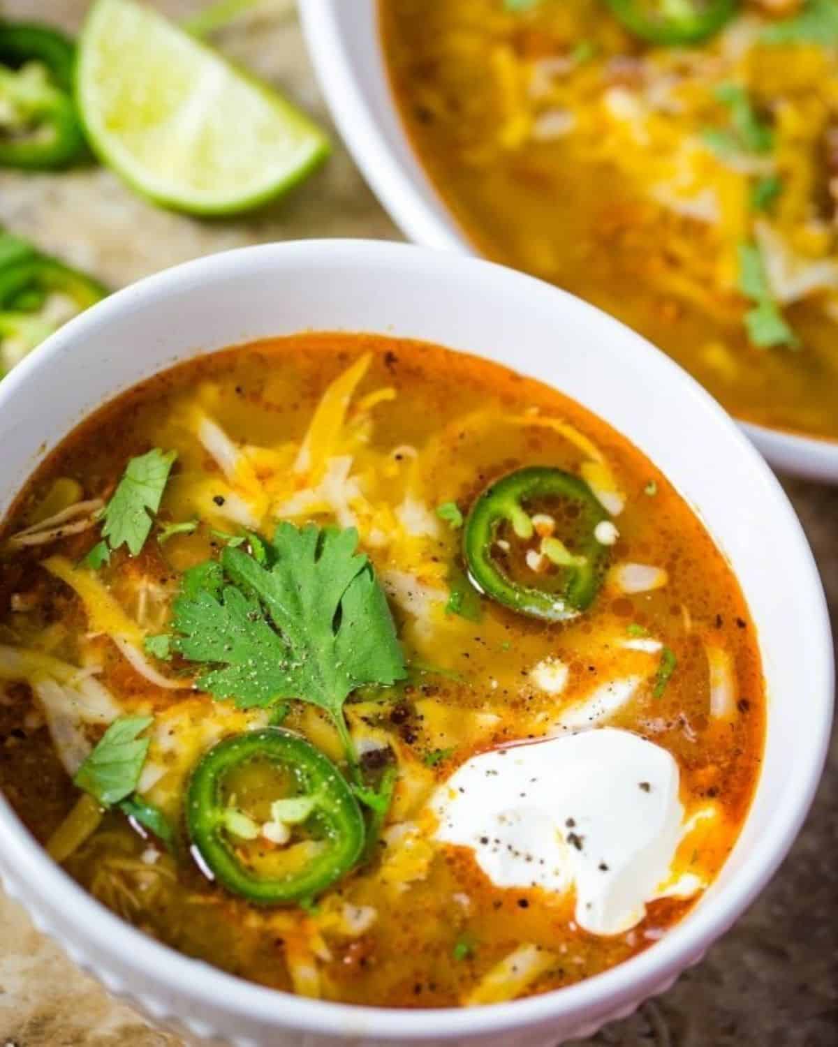Two white bowls of enchilada soup topped with jalapeños and cilantro.