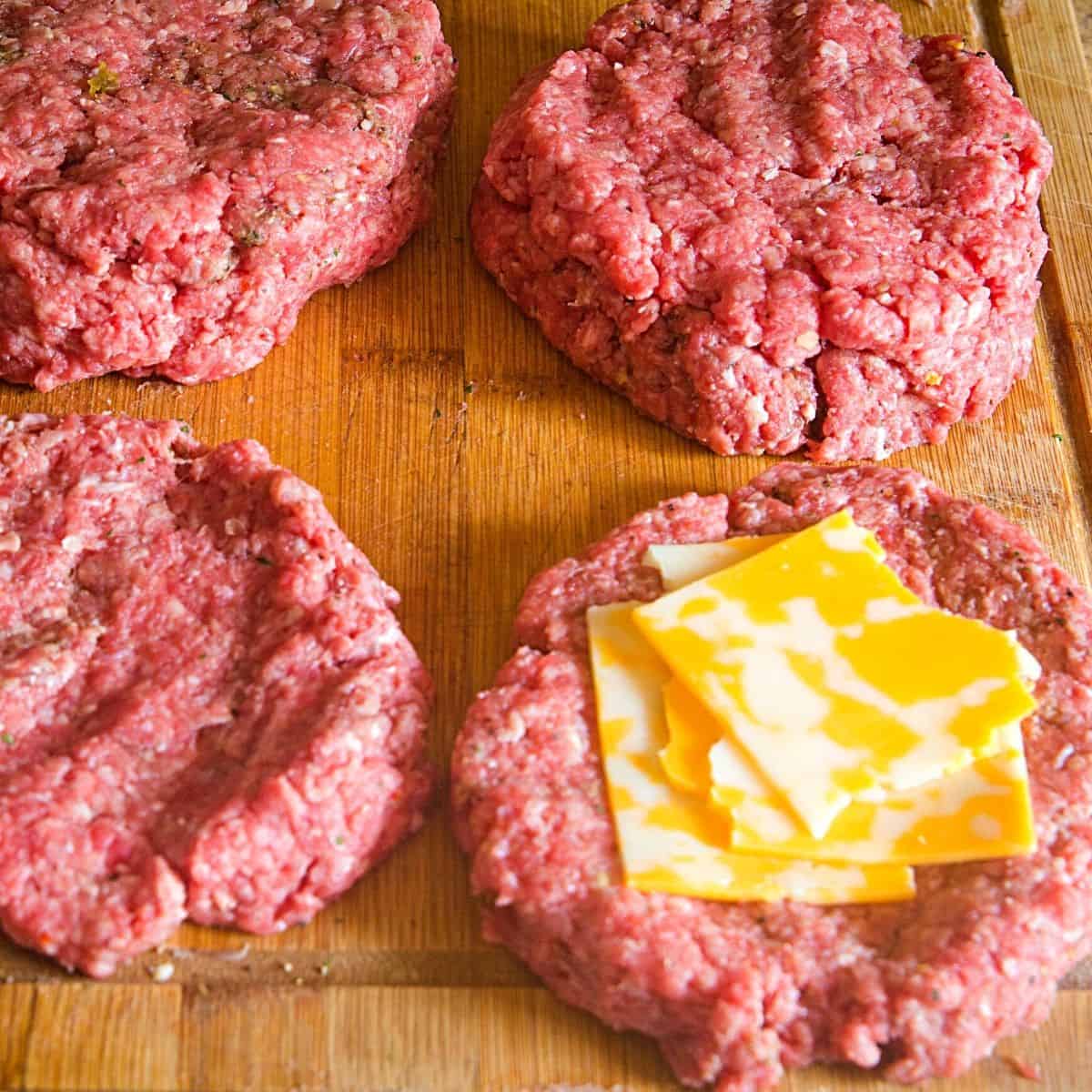 Four beef patties that have colby jack cheese in the center for juicy lucy burgers.