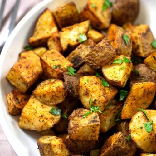 Crispy roasted potatoes with fresh seasonings and parsley in a white bowl.