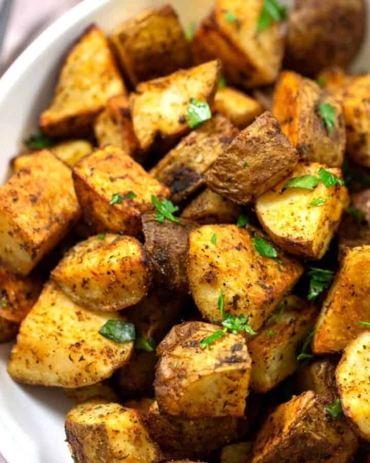 Crispy roasted potatoes with fresh seasonings and parsley in a white bowl.