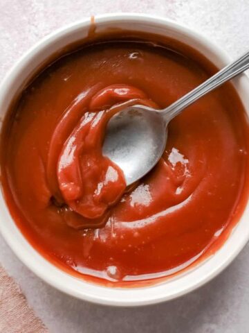 An overhead view of caramel sauce in a bowl with a silver spoon in the sauce.