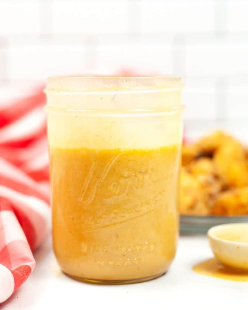 A side view of a yellow sauce in a mason jar.