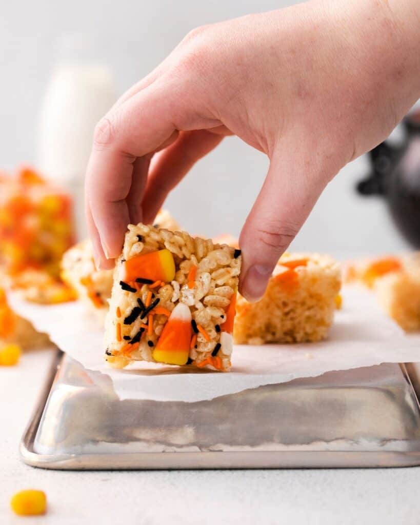 A hand holding a cereal treat with candy corn and halloween sprinkles.