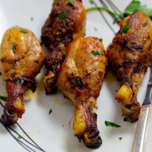Four baked chicken drumsticks on a white plate topped with chopped parsley.