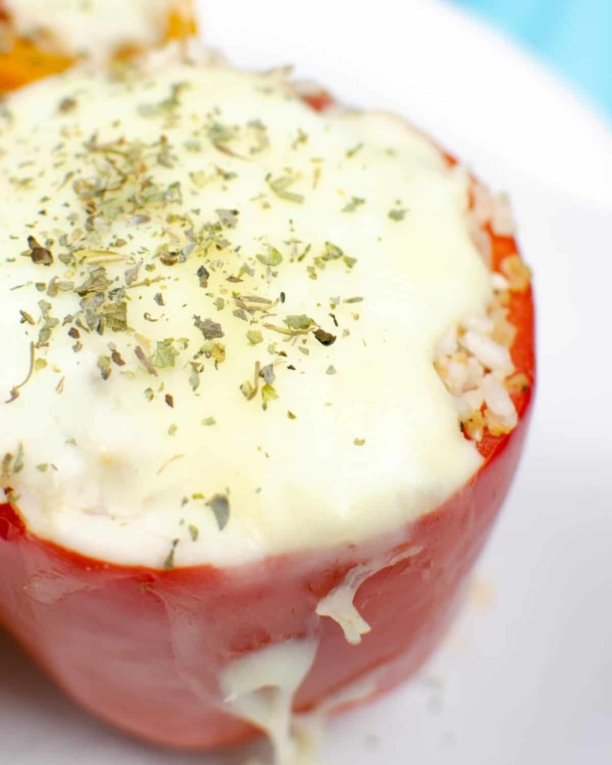 A red pepper on a white plate stuffed with rice and topped with melted cheese and Italian seasoning.