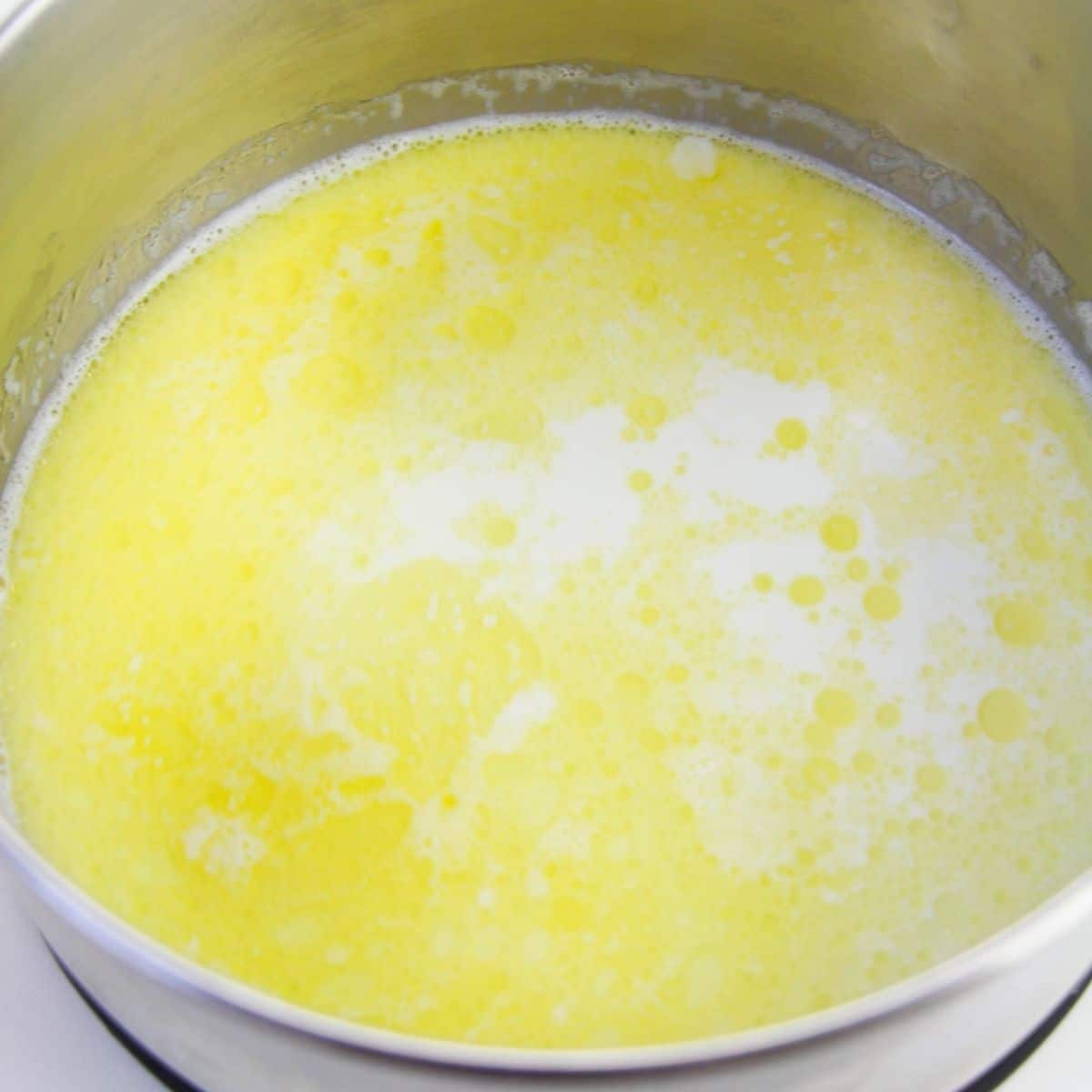 A silver mixing bowl with a yellow mixture in it. 
