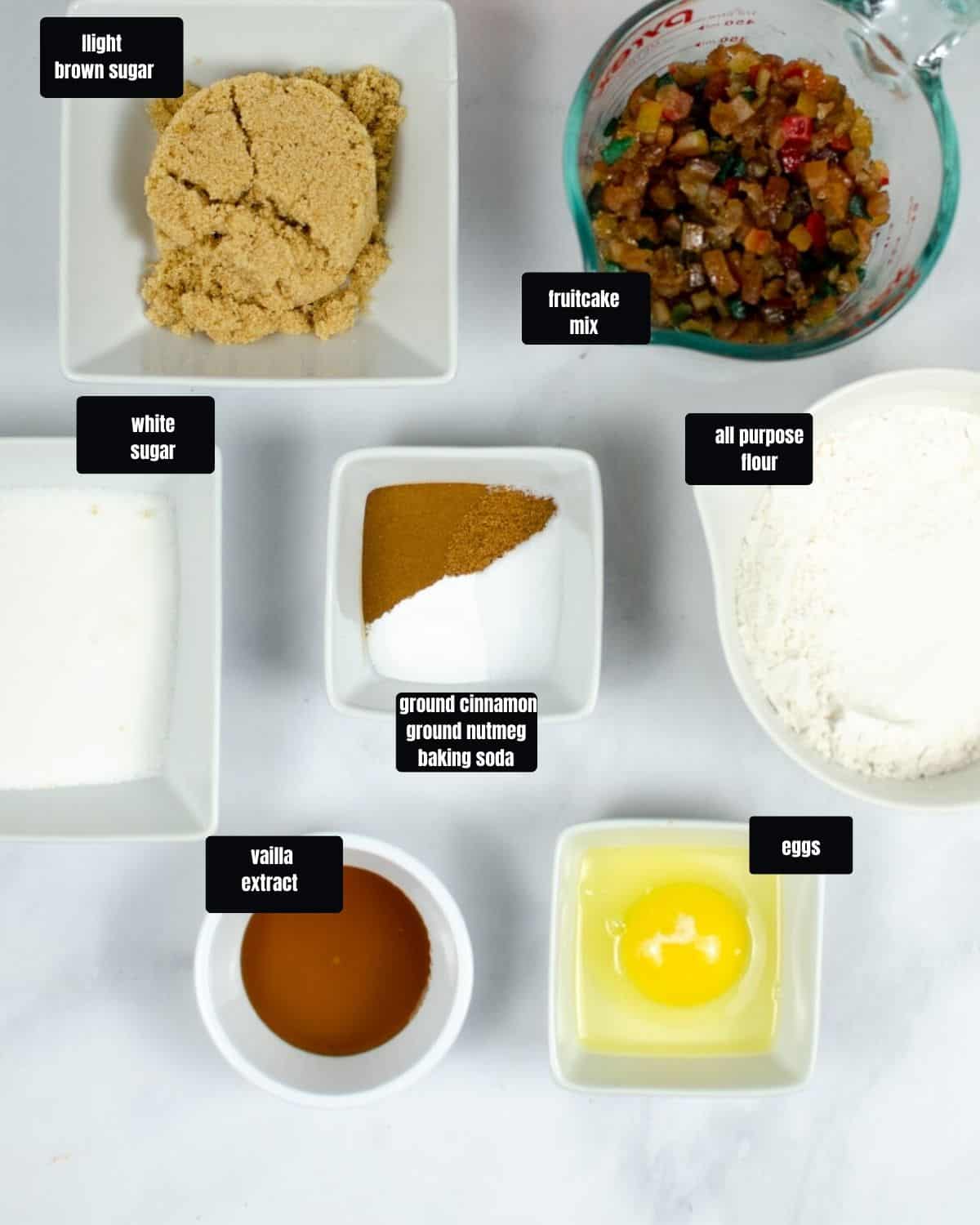 Ingredients to make fruitcake cookies in bowls on a white table.