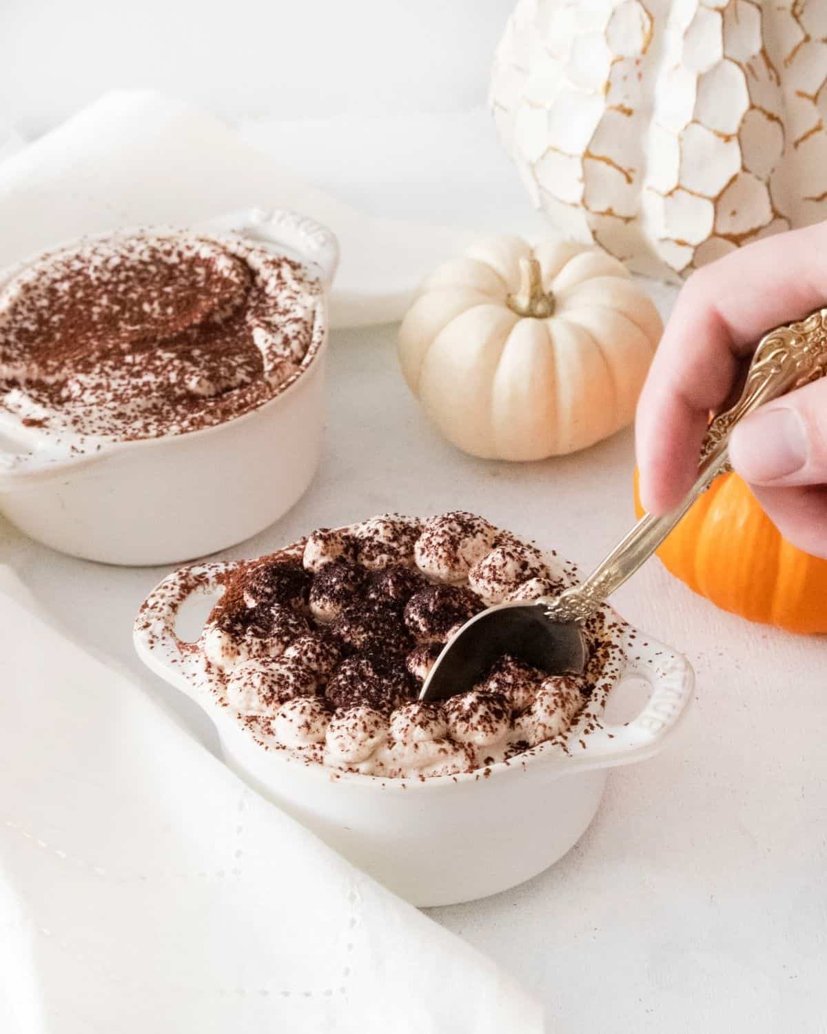 Pumpkin Tiramisu in white ramekins topped with cocoa powder and a soon in the center of one of the bowls.