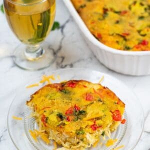 A glass plate with yellow cornbread, peppers, and chicken with the white casserole dish behind the plate.