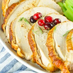 Sliced smoked turkey in a white plate topped with cranberries and rosemary pieces.