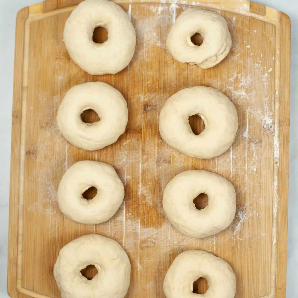 Dough formed into bagel shapes resting on a board waiting to be placed in the air fryer. 