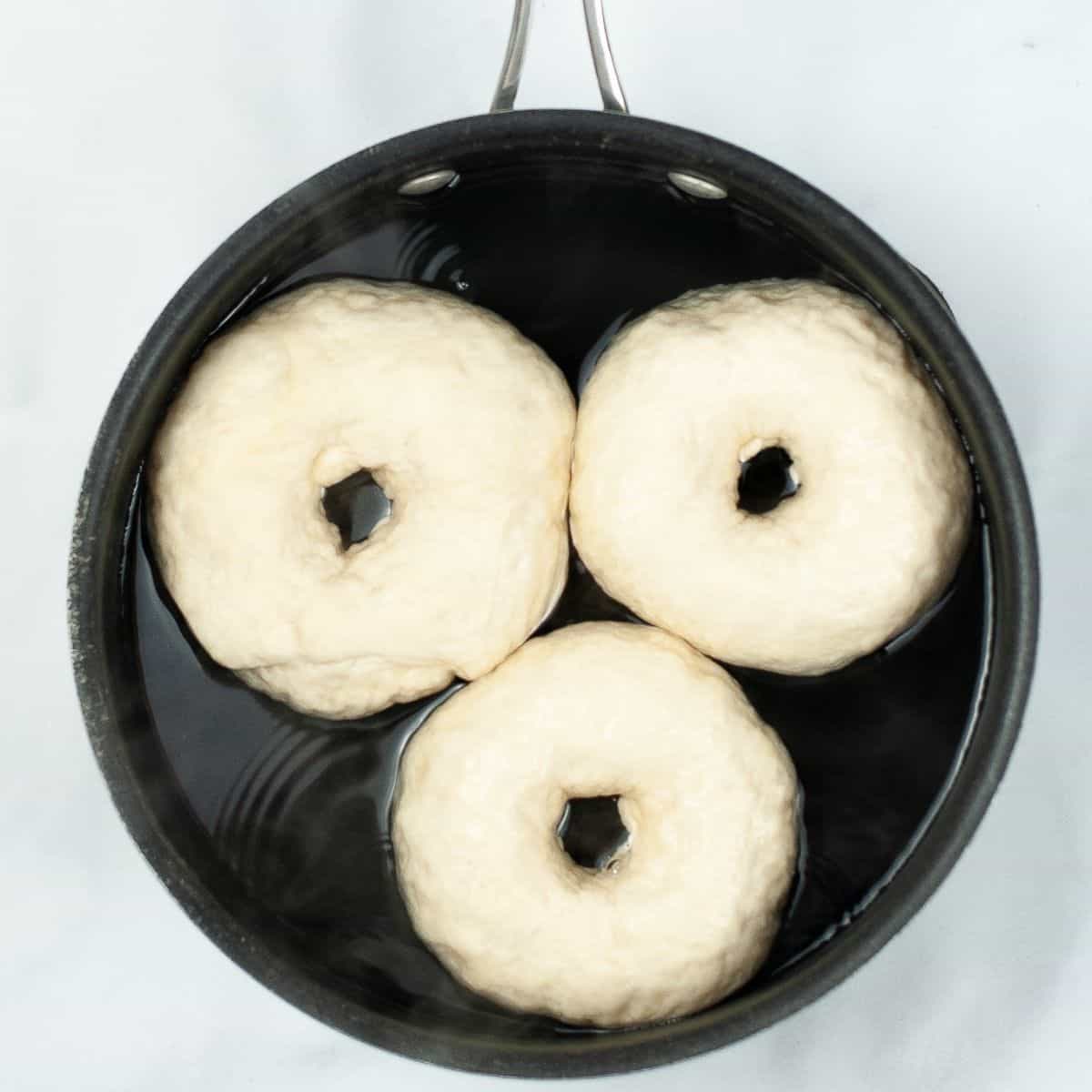 Bagels in a large bowl of water cooking. 