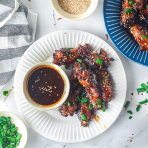 An overhead view of a white plate with chicken wings on it covered with a glaze and sesame seeds.