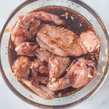A glass bowl of chicken wins marinating in a soy sauce/
