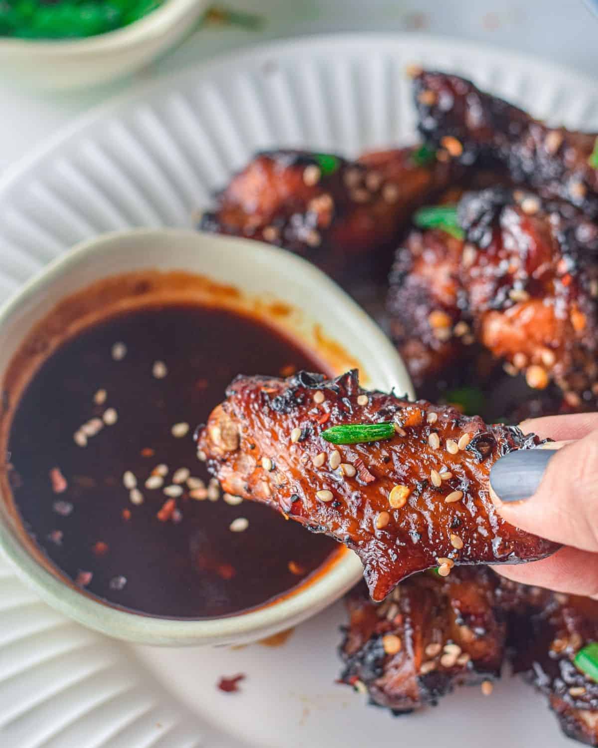 A bowl of asian sauce with a chicken wing being dipped into the sauce.