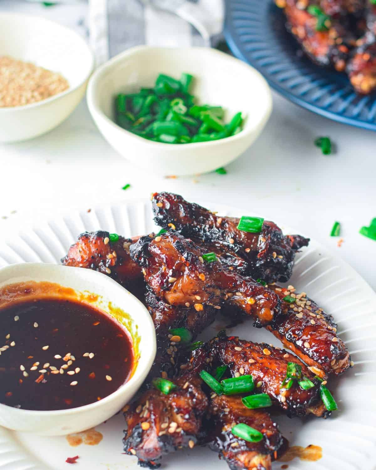 Asian marinated chicken wings on a white plate with a dipping sauce on the side.