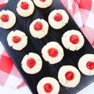 Rows of shortbread cookies on a black tray on top of a red and white checkered linen.