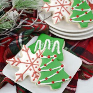 A white square plate with 3 decorated cookies with frosting and decorations.