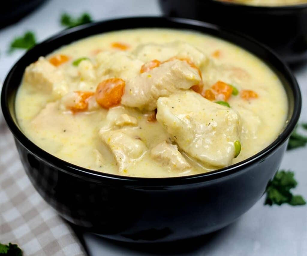 A black bowl with a creamy soup with chicken, carrots, and peas with dumplings.