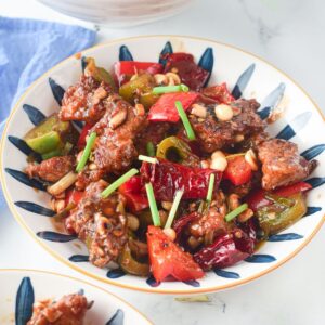 A bowl with yellow trim filled with sauteed red peppers, green peppers, chicken, garlic, and roasted nuts.