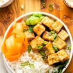 A white bowl with white rice, carrot slices, and cubed tofu topped with sesame seeds.