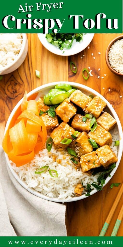 A white bowl with white rice, carrot slices, and cubed tofu topped with sesame seeds.
