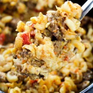 Ground beef, noodles, tomatoes on a spoon over a crockpot.