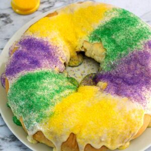 An overhead view of a round cake with white icing and purple, green, and yellow sprinkles.